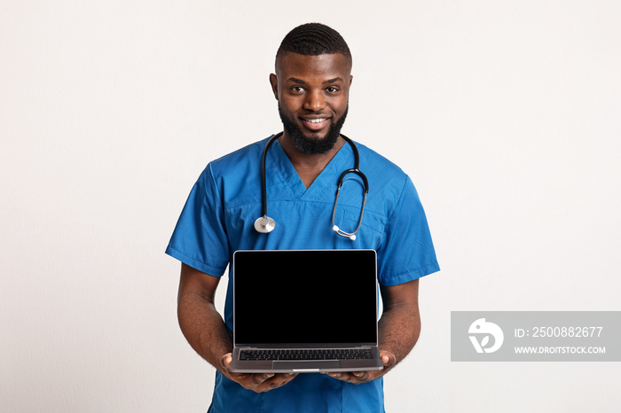 Black cheerful surgeon holding blank laptop screen