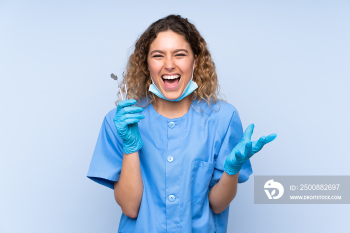 Young blonde woman dentist holding tools isolated on blue background unhappy and frustrated with something