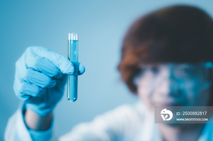 Scientist hand hold test tubes filled with blue sample chemicals in chemistry science laboratory. Glassware in medical research. Scientific lab for Biotechnology.