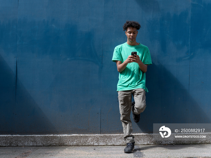 Young man using phone against blue wall