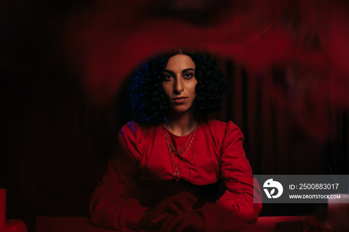 young fortune teller looking at camera on dark background with red smoke.