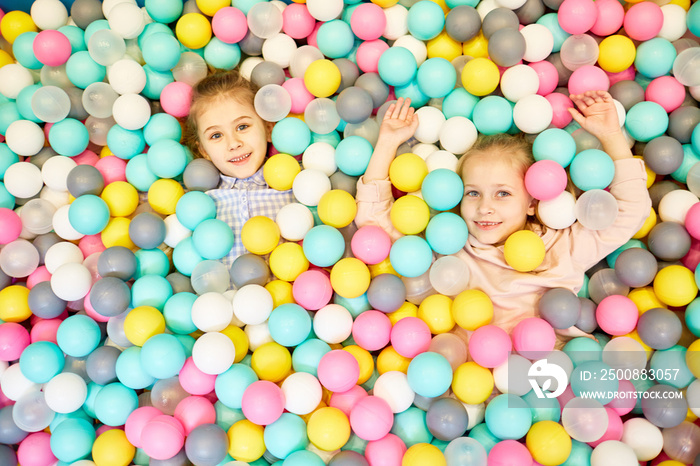 Two adorable friendly girls playiing in heap of colorful balloons at birthday party