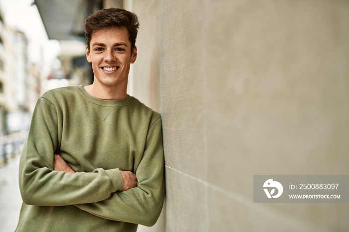 Young hispanic man smiling happy with arms crossed gesture at the city.