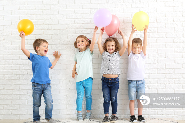 Cute little children with air balloons near white brick wall