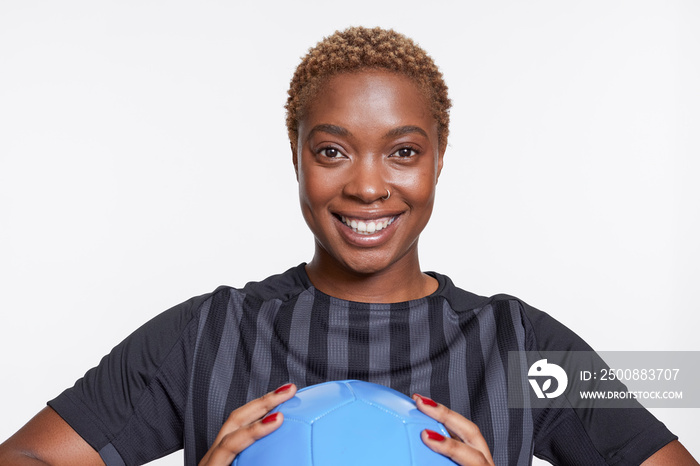 Studio portrait of smiling female soccer player with ball