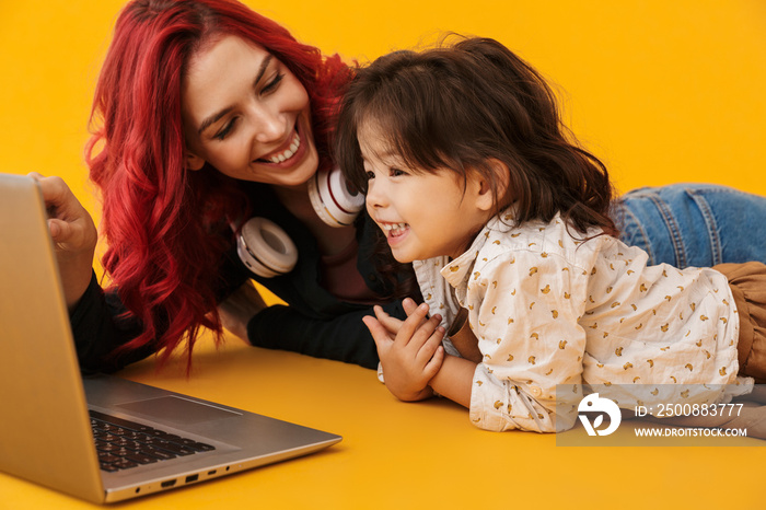 Image of smiling lovely woman and her daughter using laptop