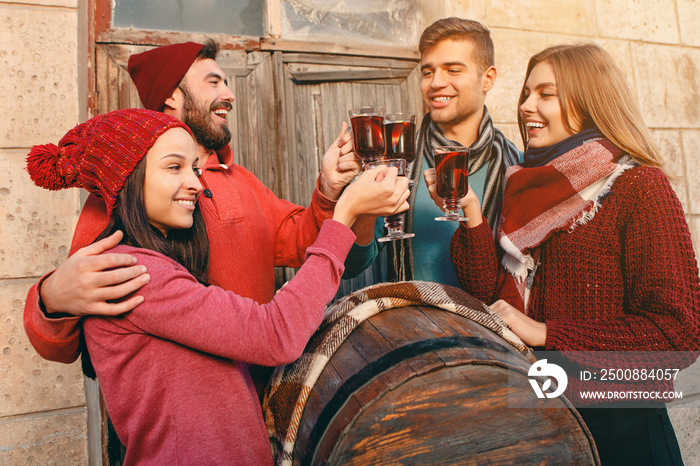 Smiling european men and women during party photoshoot. The guys posing as friends at studio fest with wineglasses with hot mulled wine on foreground.