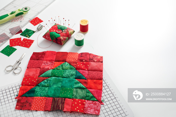 Christmas tree patchwork block, bright square pieces of fabric, pincushion, quilting and sewing accessories on white background