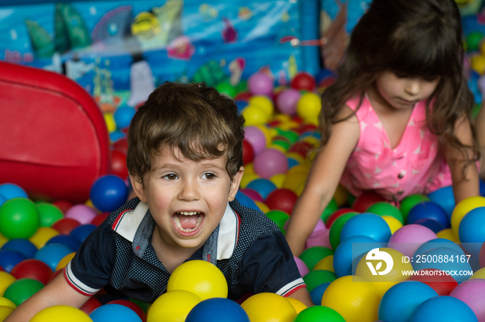 Happy children having fun at kids indoor play center. Kids playing with colorful balls in playground ball pool. Holiday, children’s party, a games room