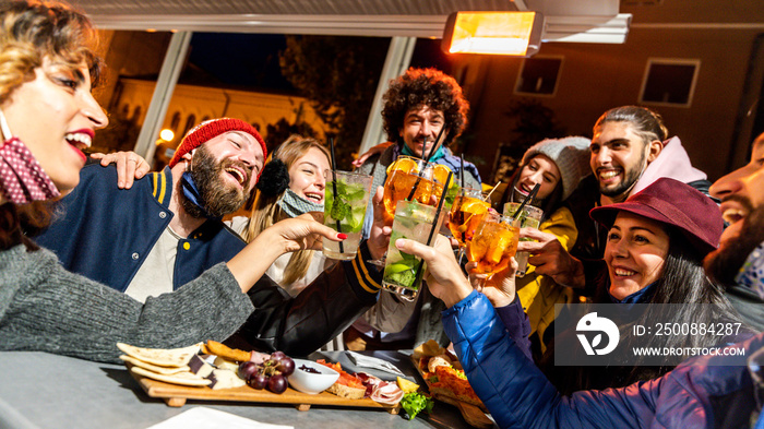 Friends group drinking cocktail bar with open face masks - Happy young people having fun together toasting glasses - New normal lifestyle concept. Focus on left glass.