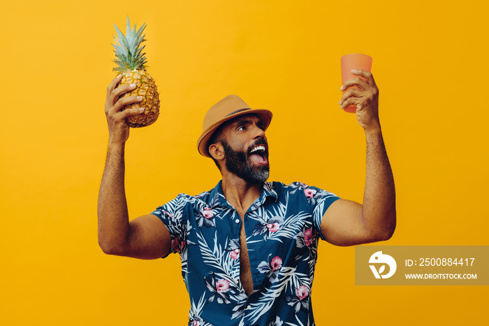 handsome excited african american man wearing Hawaiian shirt and hat with pineapple and glass looking away mid adult studio shot