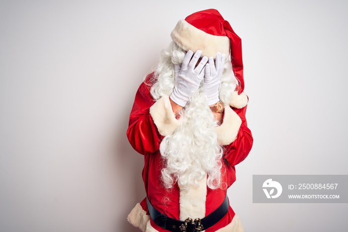 Middle age handsome man wearing Santa costume standing over isolated white background with sad expression covering face with hands while crying. Depression concept.