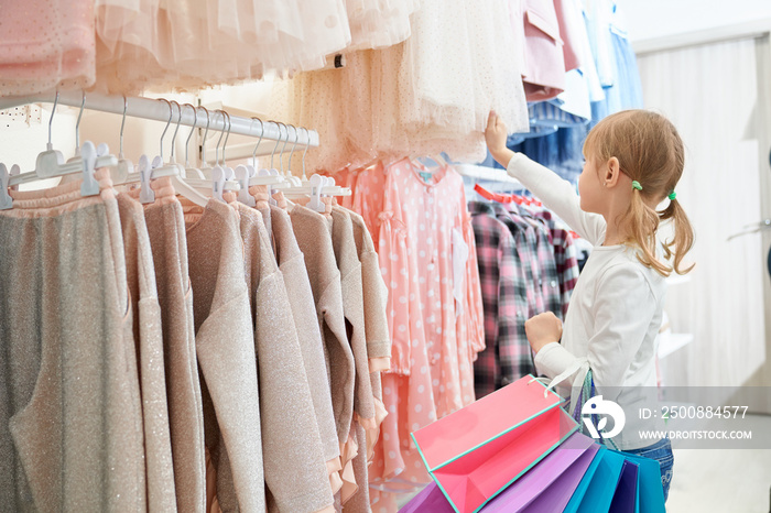 Little customer standing in store and choosing new dresses