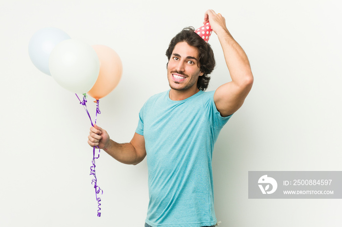 Young caucasian man holding balloons celebrating a brithday isolated in a grey background