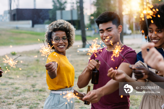 Happy young friends having fun in party celebration - Group of young adult men and women laughing together holding fire sparkles