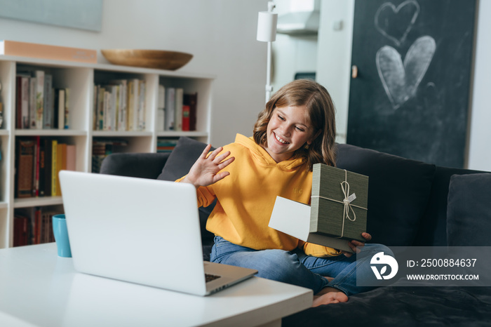 young girl opening gift and using laptop for video call at home