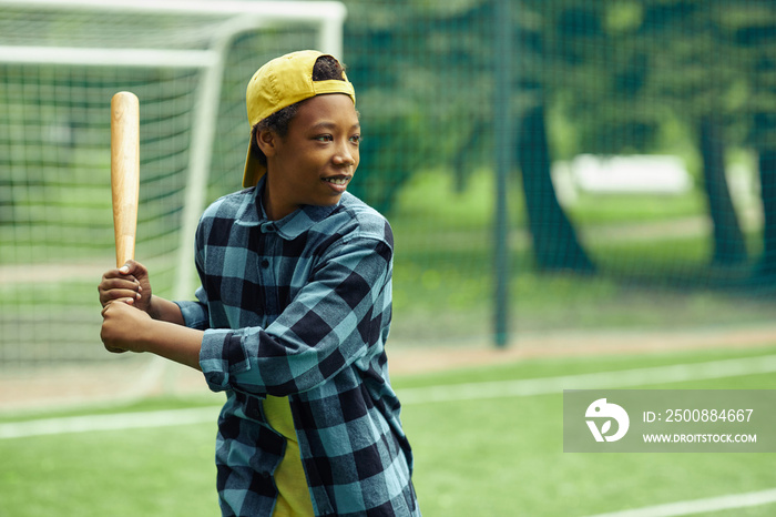 African boy in cap standing with bat and ready to hit the ball during baseball game outdoors