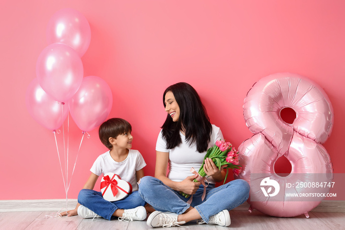 Little son and his mother with gift, bouquet of flowers for International Women’s day and balloons on color background