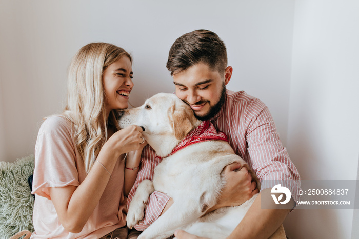 Girl in oversize shirt laughs wholeheartedly and looks at her dark-haired man holding Labrador