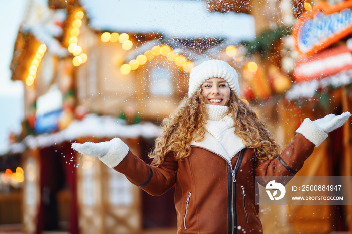 Happy smiling woman catching snowflakes, posing at festive street market. Festive Christmas fair, winter holidays concept.