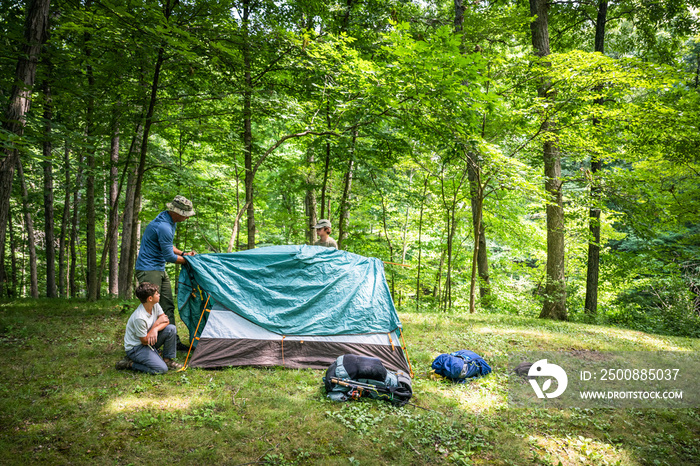 Air Force service member sets up a tent with his sons on  a backpacking trip.