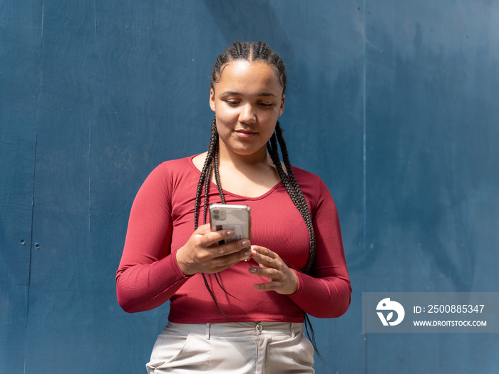 Portrait of young woman using smart phone against blue wall