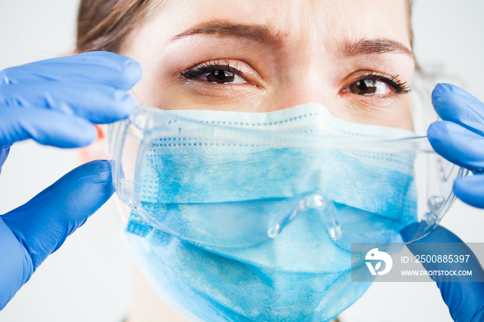 Closeup of teary eyes of female caucasian medical worker wearing blue face mask and gloves