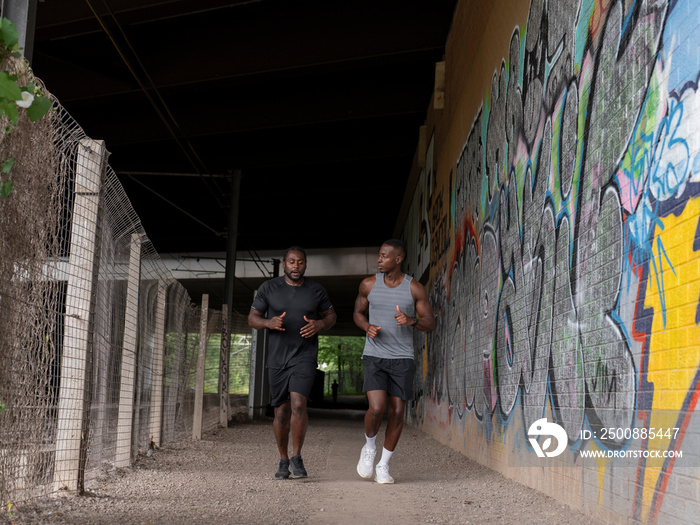 Two men jogging under bridge