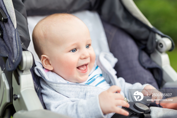 Portrait of funny baby boy laughing outdoors. Cute adorable child having fun sitting in stroller during walk