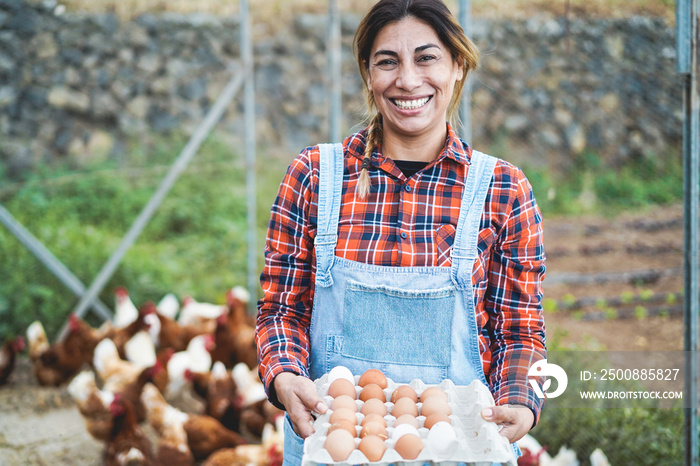 Happy farmer woman picking up organic eggs in henhouse - Farm lifestyle and healthy food concept - Focus on face