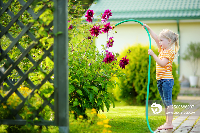 Cute little girl watering flowers in the garden at summer day.