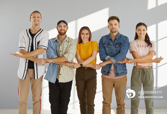 Together we stand strong. Team of happy, cheerful young people standing in row and holding hands. Studio group portrait of college friends standing in line, holding hands and smiling at camera