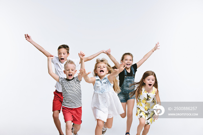 Group of fashion cute preschooler kids friends running together and looking at camera on a white studio background. The friendship, fashion, summer concept. Space for text.