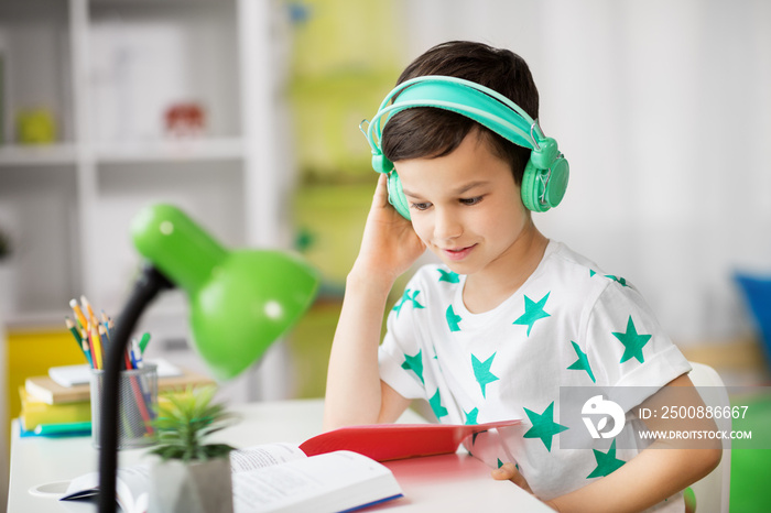 education, childhood and school concept - student boy in headphones reading book at home