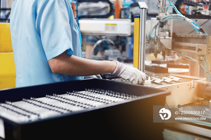 A female worker is working to control an automatic machine for an electronic circuit board product part.