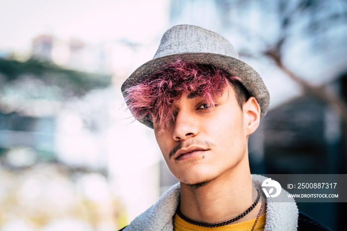 Handsome diversity young boy man portrait with violet hair and piercing on face - concept of handsome teenager with his own style trendy - outdoor city defocused background for modern hispanic people