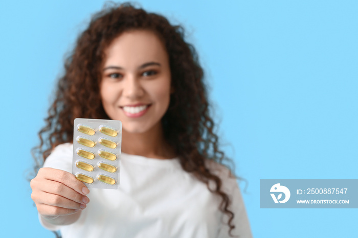 Young woman with fish oil pills on color background, closeup