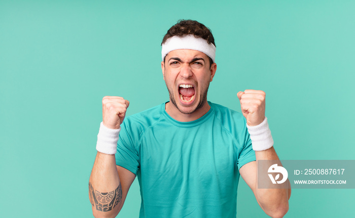 fitness man shouting aggressively with an angry expression or with fists clenched celebrating success
