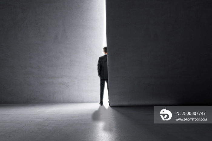 Back view of man stepping into the light from behind a concrete wall. Success and future concept.