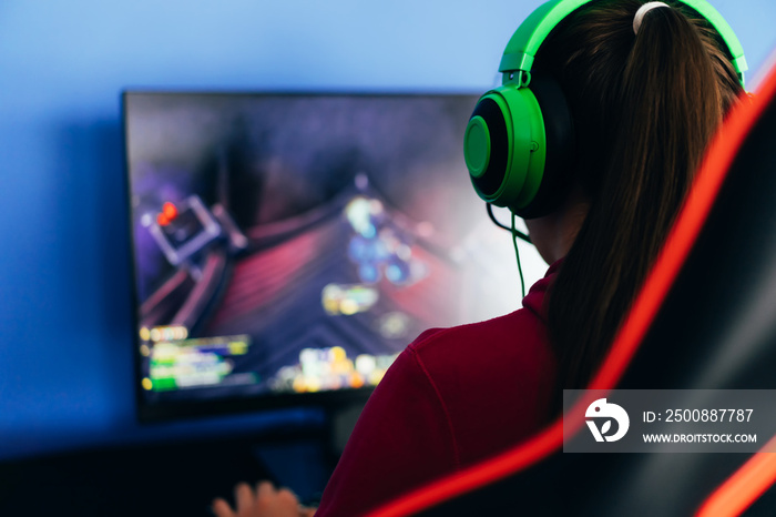 A young girl playing a computer game on professional armchair against monitor in green headphones, live stream, esports