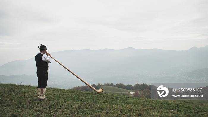 Playing the alpine horn in front of a valley in the Alps