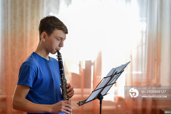 The guy plays the clarinet, looks at the music and plays music in a music school.