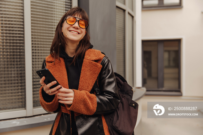 Close up view of smiling woman with backpack and holding phone look at camera