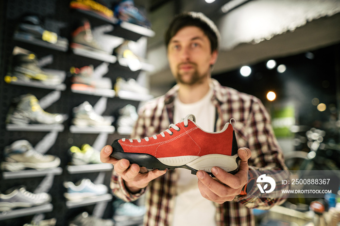 Store clerk helping customer try hiking boots at outdoors equipment shop. Salesman demonstrating trekking and hiking footwear for outdoor trails. Consultant help choose hiking boots in sports store