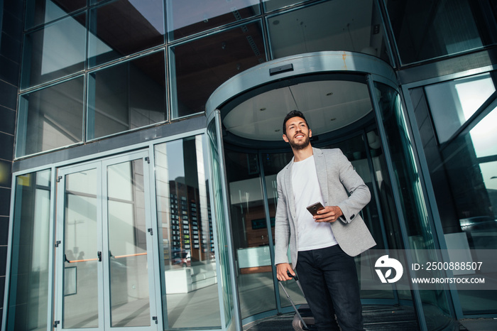 Businessman walking from hotel lobby. Full length portrait of young executive with a suitcase.