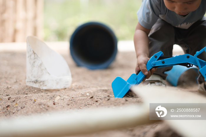 Asian boy playing with soil and sand by excavator toy