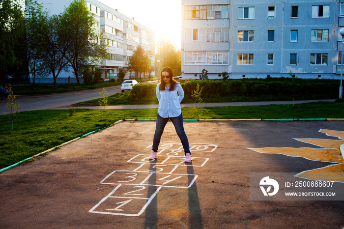 Cute girl playing hopscotch. Sunset. Beautiful summer, rest after work in the courtyard of a multi-storey building