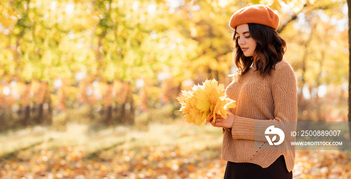 Happy young woman in autumn park holding yellow leaves. Warm autumn weather. Fall concept. Copy space.