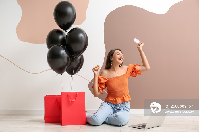 Happy young woman with credit card, laptop and shopping bags on color background. Black Friday sale