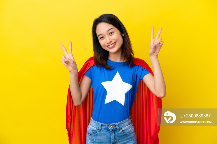 Super hero Vietnamese woman isolated  on yellow background showing victory sign with both hands